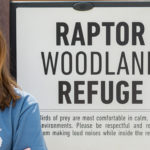 Picture of a woman with a sign in the backround that says "raptor woodland refuge"