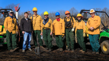 a collection of people most of whome have hard hats, yellow jackets, brown boots, and green pants.