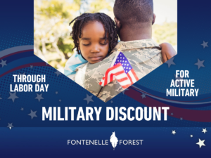 A picture of a member of the military holding a child. Framed in blue with white text, "THROUGH LABOR DAY FOR ACTIVE MILITARY MILITARY DISCOUNT" with the Fontenelle Forest logo