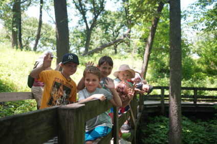 A picture of a group of smiling children standing on Fontenlle Forest's boardwalk, looking over the railing and waving at the camera.