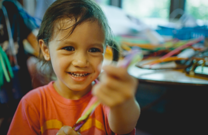 A picture of a smiling young girl playing with pipe cleaners.